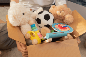 A guy holding a box full of toys and stuff toys